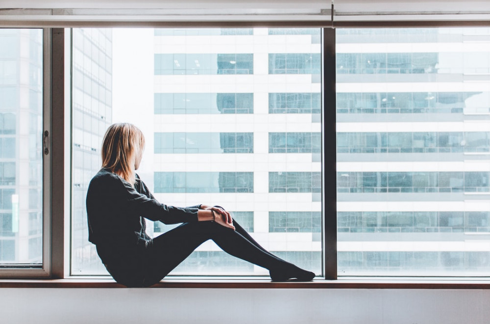 Girl looking out of her apartment window, wondering, 'Can I Make money blogging about my life?'.